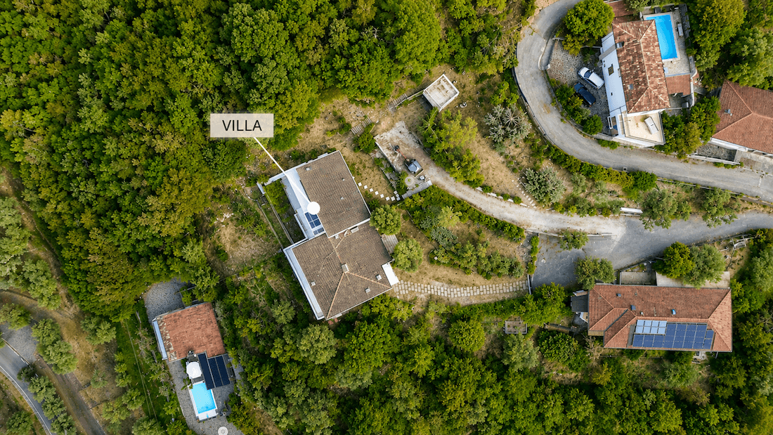 Luftaufnahme der Villa mit braunem Dach, eingebettet in eine grüne Landschaft mit weiteren Häusern und Pools.
