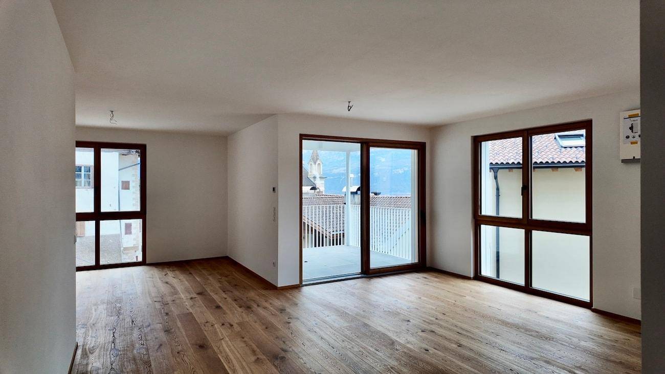 Geräumiger Wohnbereich mit Holzboden, weißen Wänden und mehreren großen Fenstern für viel Licht.
