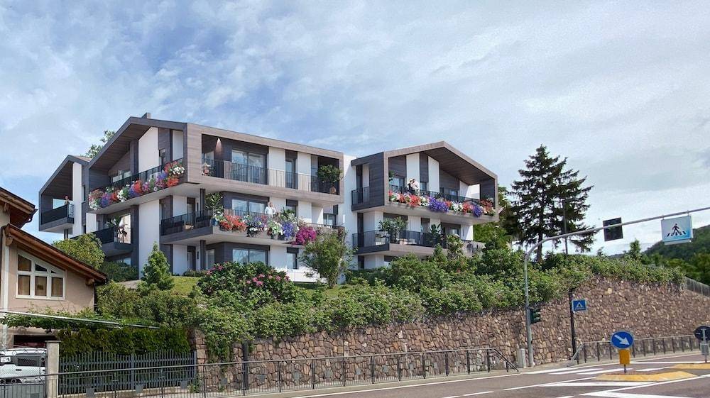 Moderne Wohnanlage mit Balkonen und Blumenkästen in einer grünen, bergigen Umgebung.