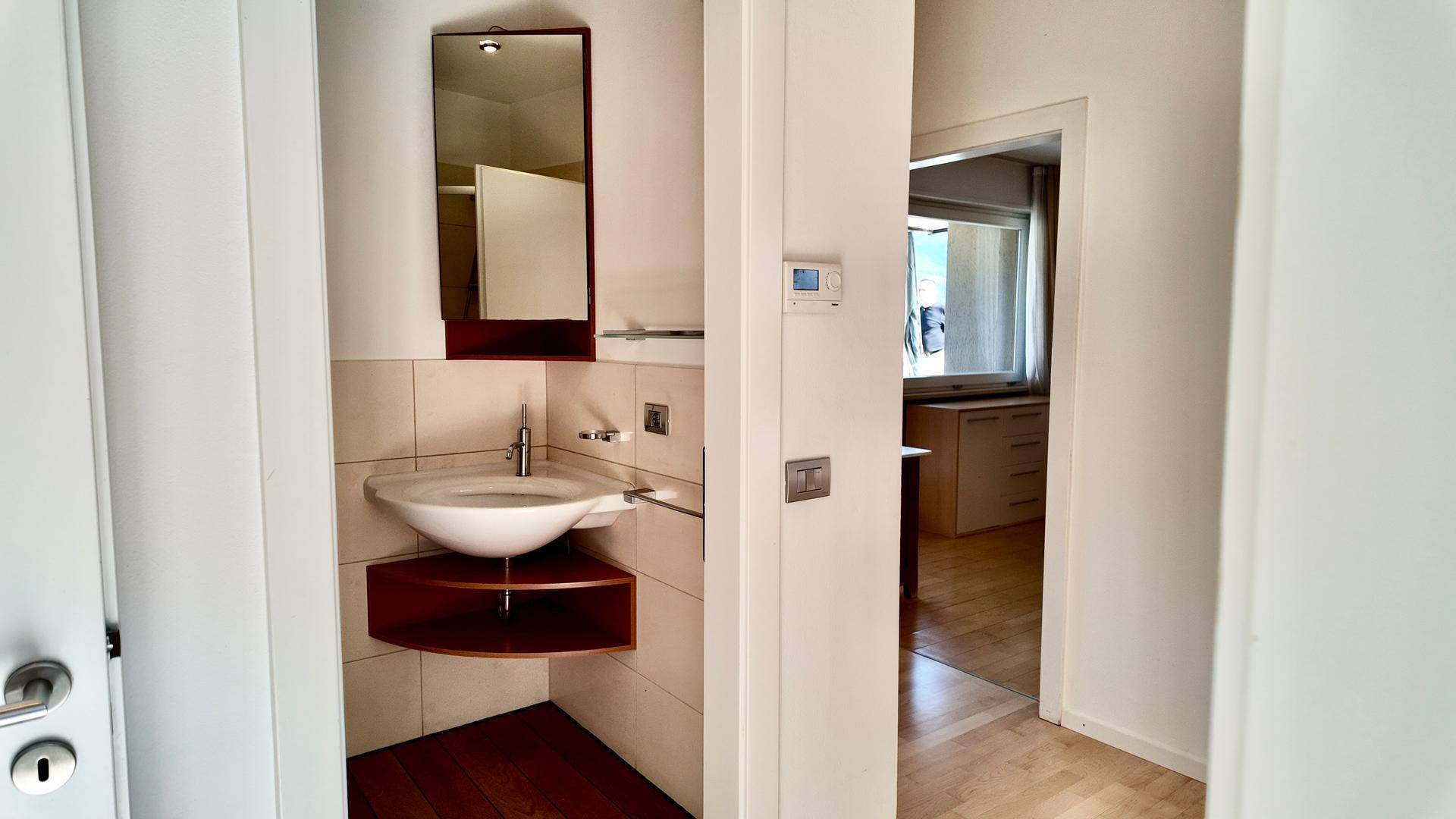 Kleines Gäste-WC mit Eckwaschbecken und Spiegel, angrenzend an einen Flur.