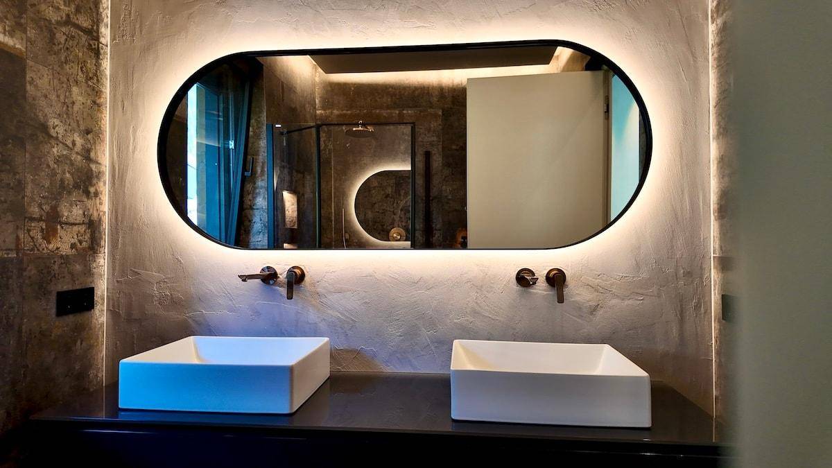Elegantes Badezimmer mit großem beleuchtetem Spiegel, zwei Aufsatzwaschbecken und modernen Armaturen.