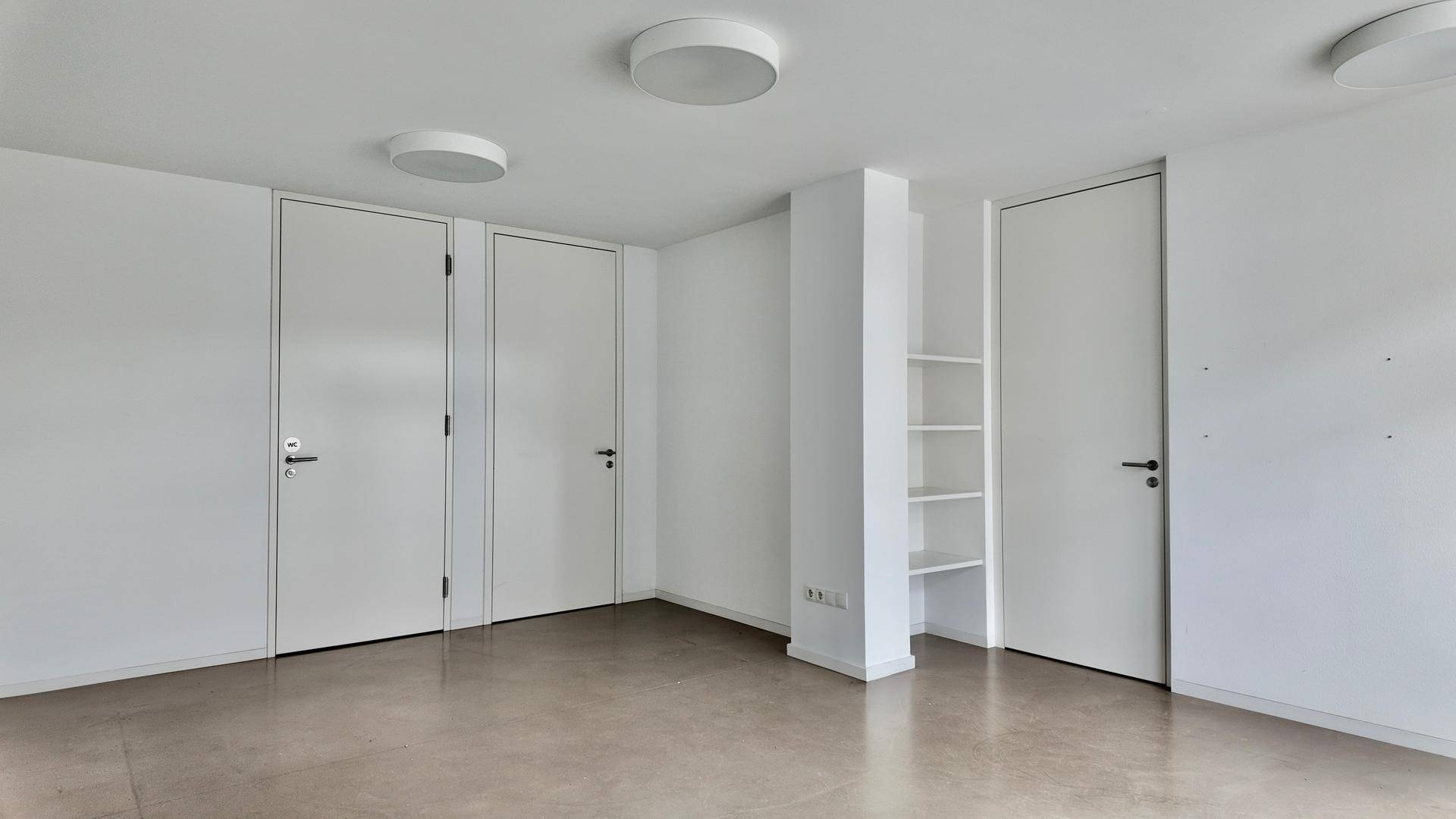 Geräumiger Innenraum mit mehreren weißen Türen und einem praktischen eingebauten Regal an der Wand.