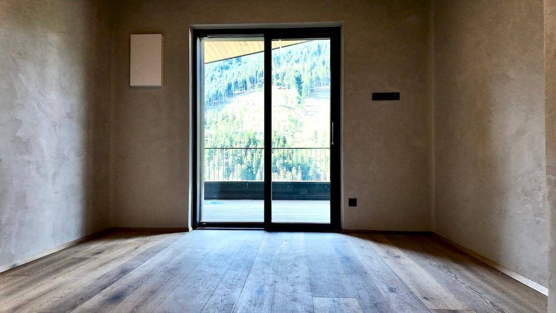 Heller Raum mit Holzboden und Schiebetür, die einen weiten Blick auf die Berge bietet.
