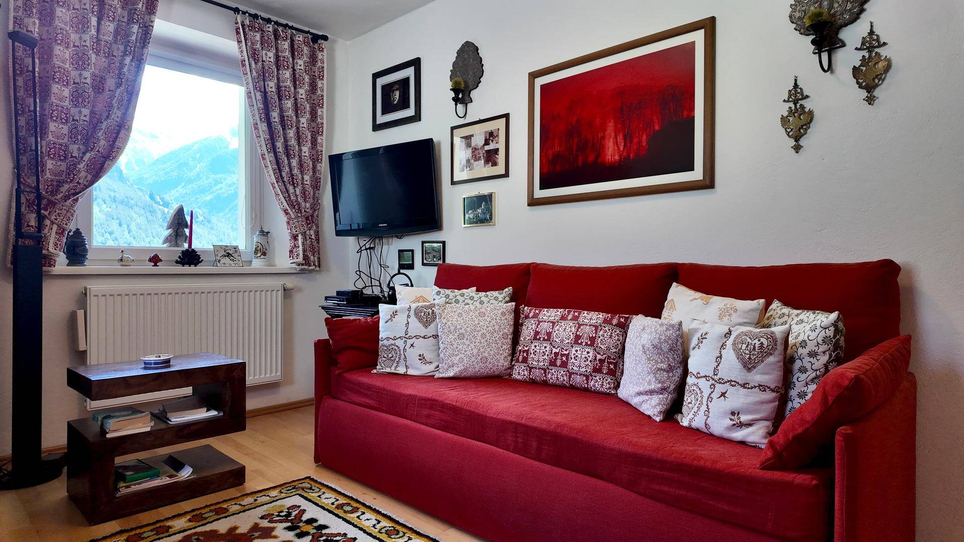 Wohnzimmer mit bequemen roten Sofas, Fernseher und dekorativen Bildern an den Wänden.