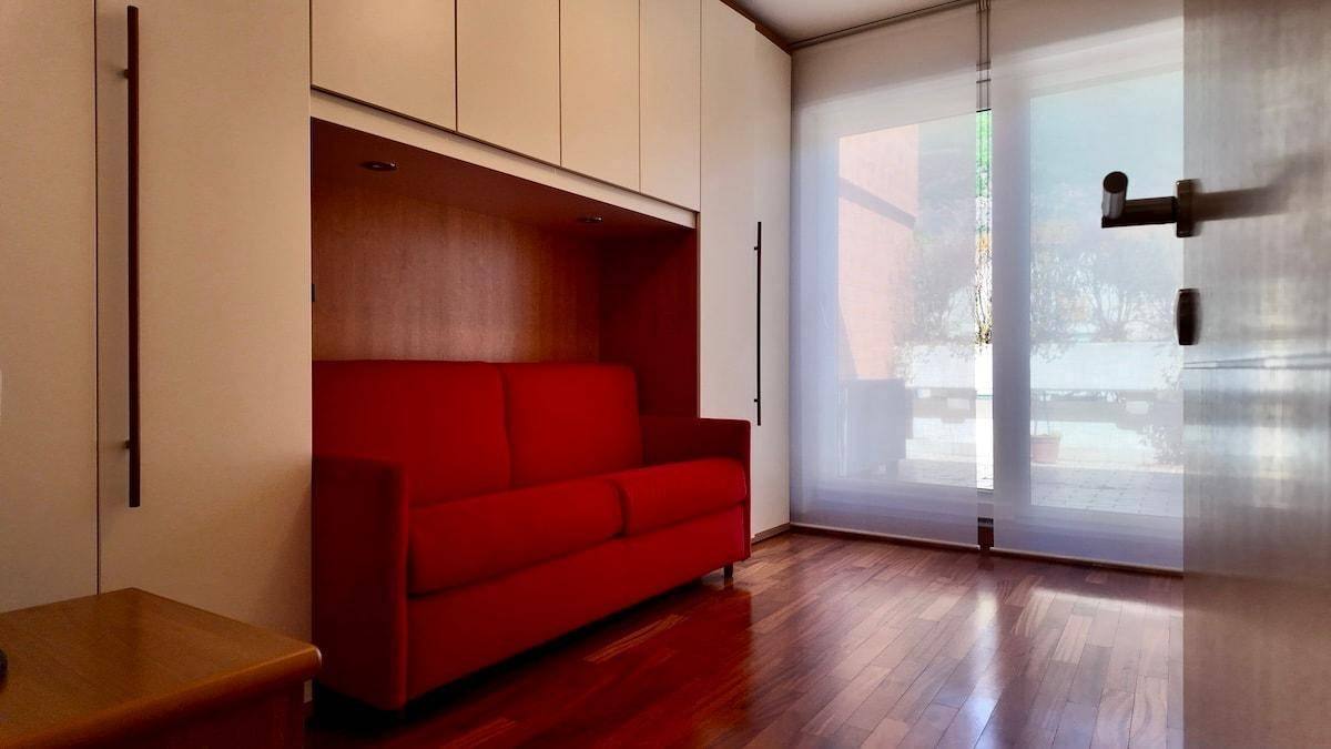 Wohnbereich mit rotem Sofa, Holzboden und Einbauschränken, hell durch Fenster.