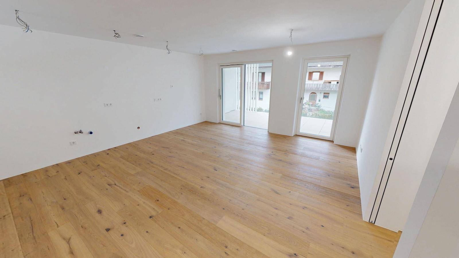 Weitläufiger, leerer Raum mit Holzboden und mehreren Zugängen zu Außenbereichen.