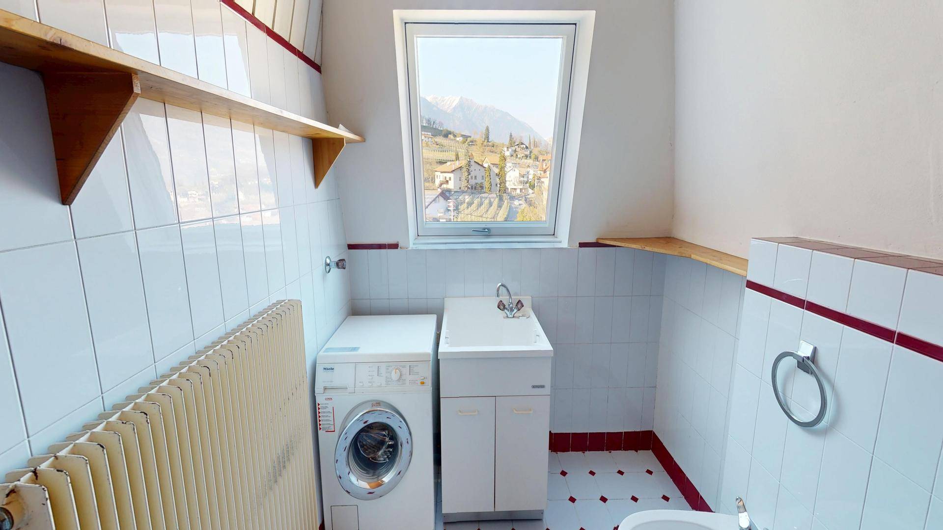 Badezimmer mit Waschmaschine, Waschbecken und Dachfenster mit Bergblick.