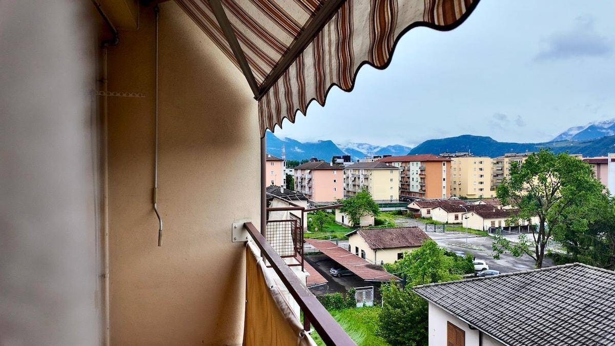 Balkon mit Markise und Blick auf Wohngebäude sowie die umliegenden Berge.