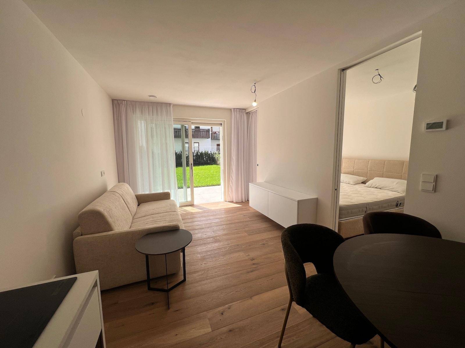 Offener Wohn- und Essbereich mit Holzboden und Blick auf den Garten sowie das Schlafzimmer.