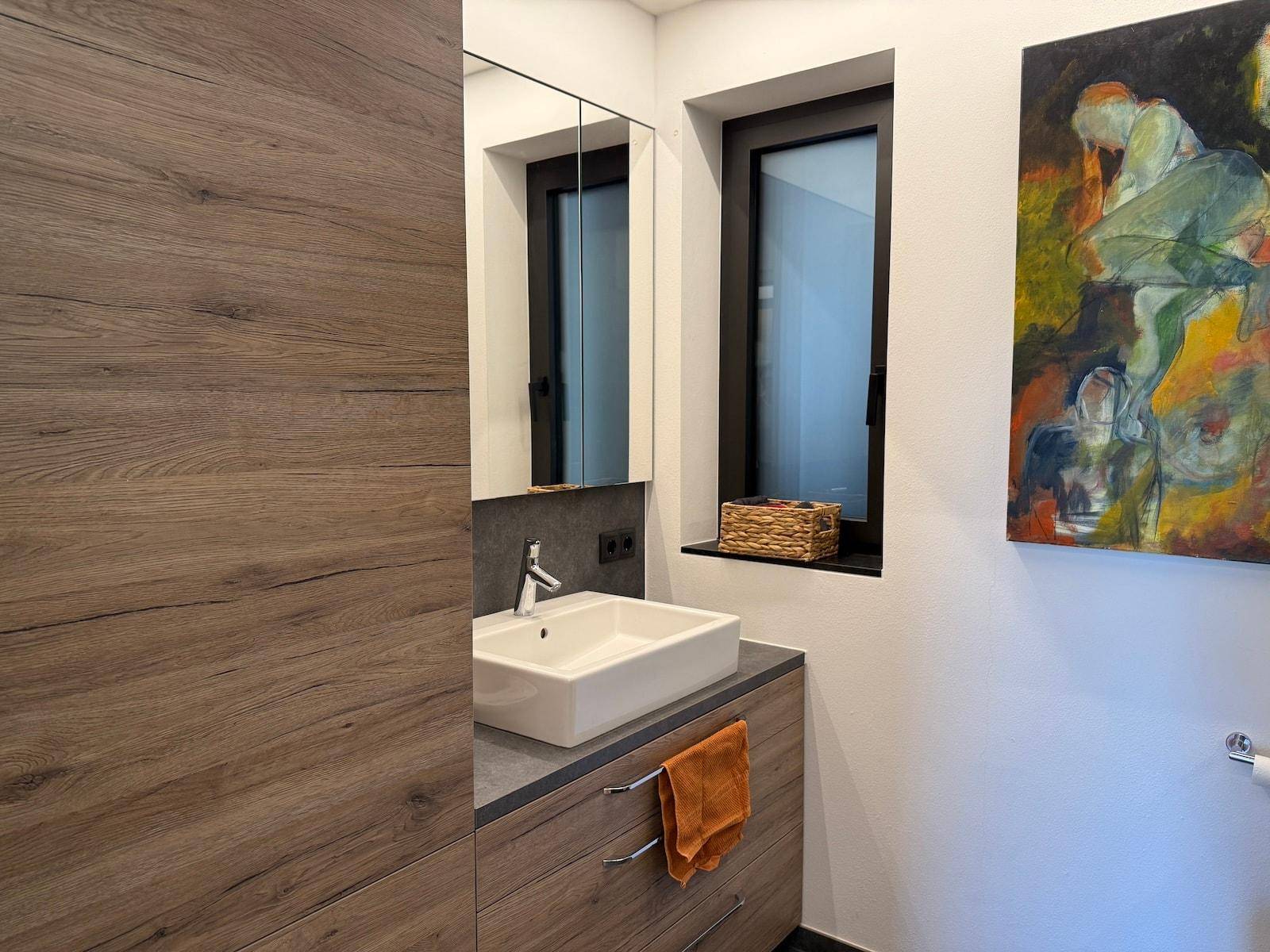 Modernes Badezimmer mit Holzwaschtisch, rechteckigem Waschbecken und einem Fenster.