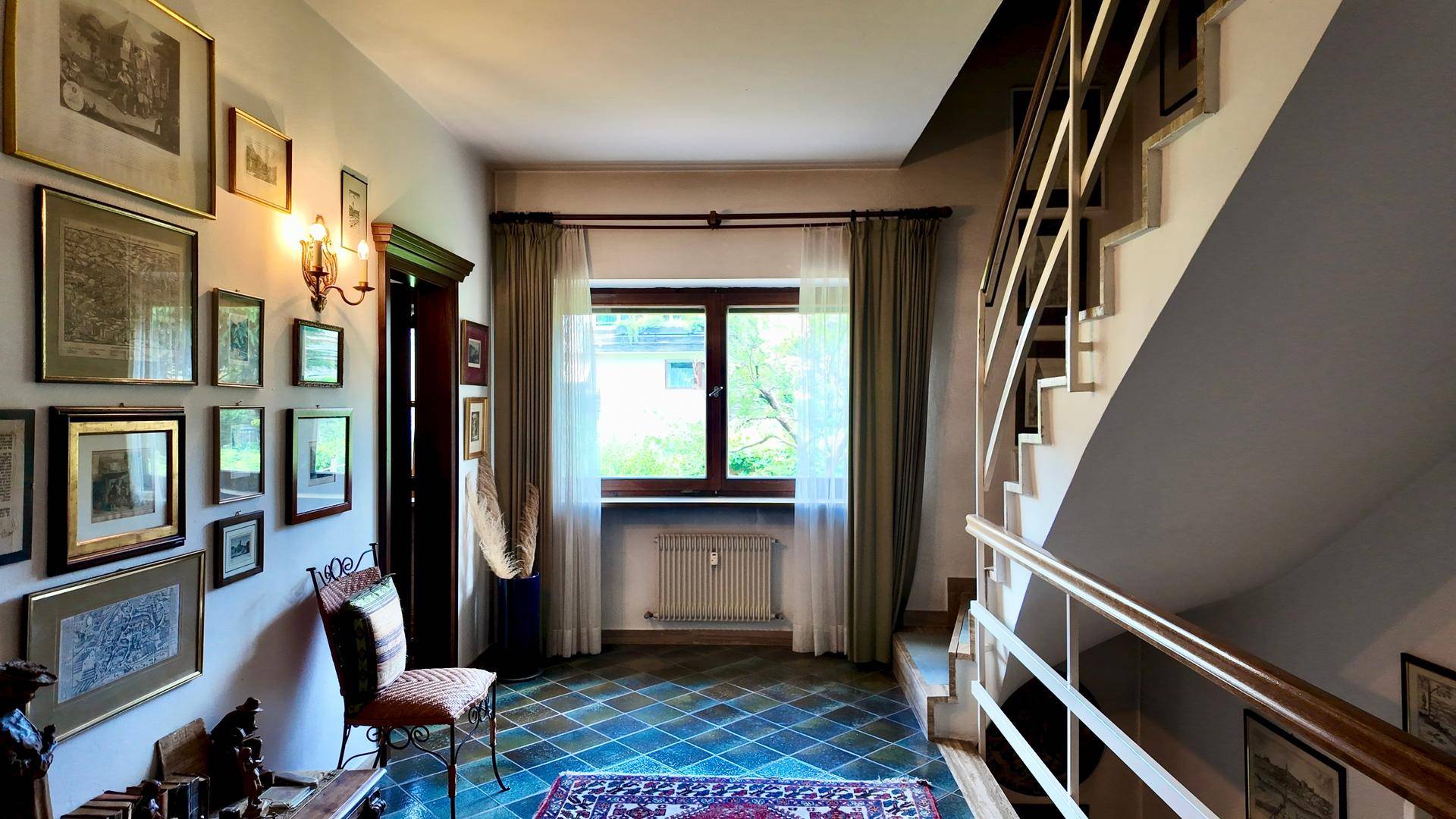 Heller Flur mit gefliestem Boden, Treppe und Fenster mit Blick ins Grüne.