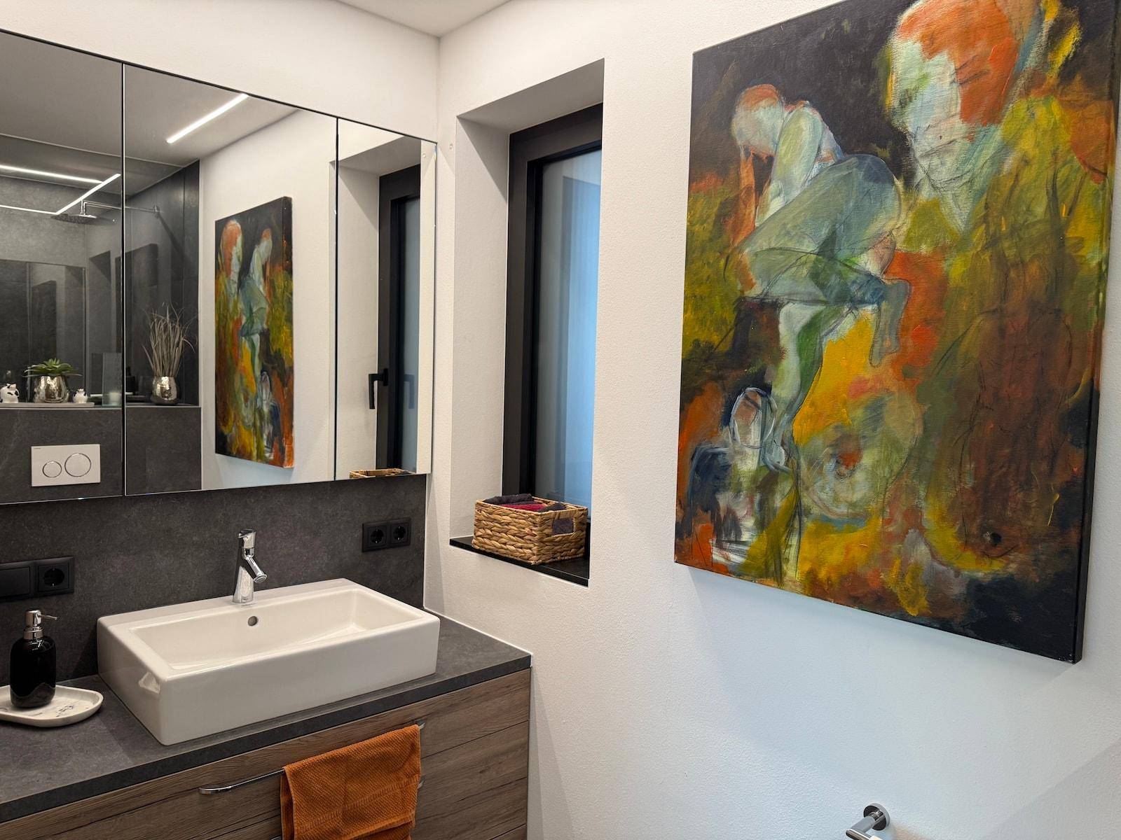 Helles Badezimmer mit modernem Waschtisch, Spiegelschrank und einem farbenfrohen Kunstwerk.