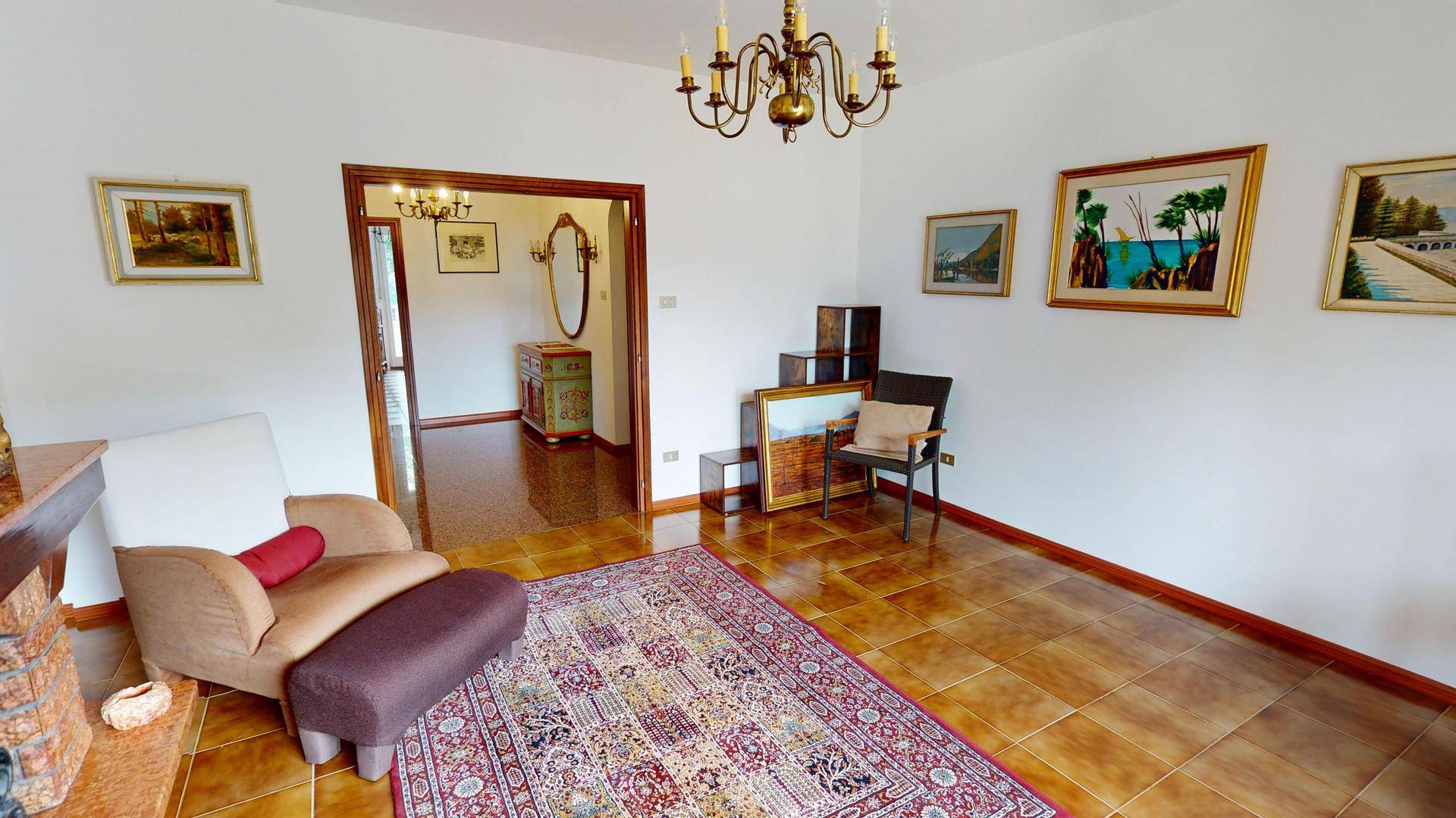 Geräumiges Wohnzimmer mit Fliesenboden, Kronleuchter und traditionellen Gemälden an den Wänden.