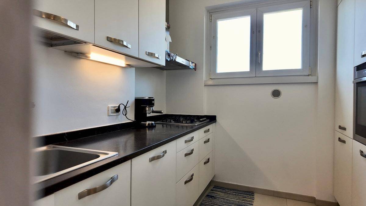 Funktionale Küche mit weißen Schränken, dunkler Arbeitsplatte und Gasherd unter einem Fenster.