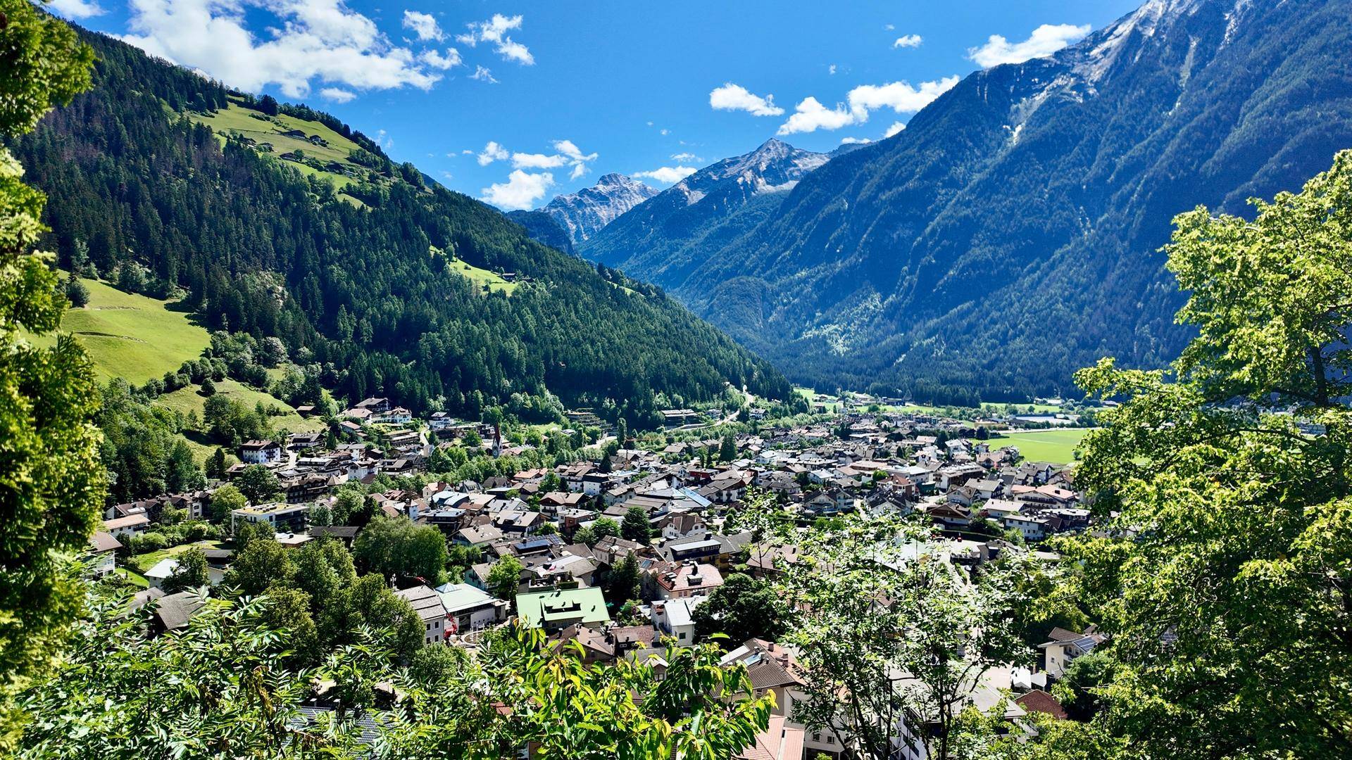 Weitläufiger Panoramablick auf ein malerisches Alpental mit einem charmanten Dorf und majestätischen Bergen.
