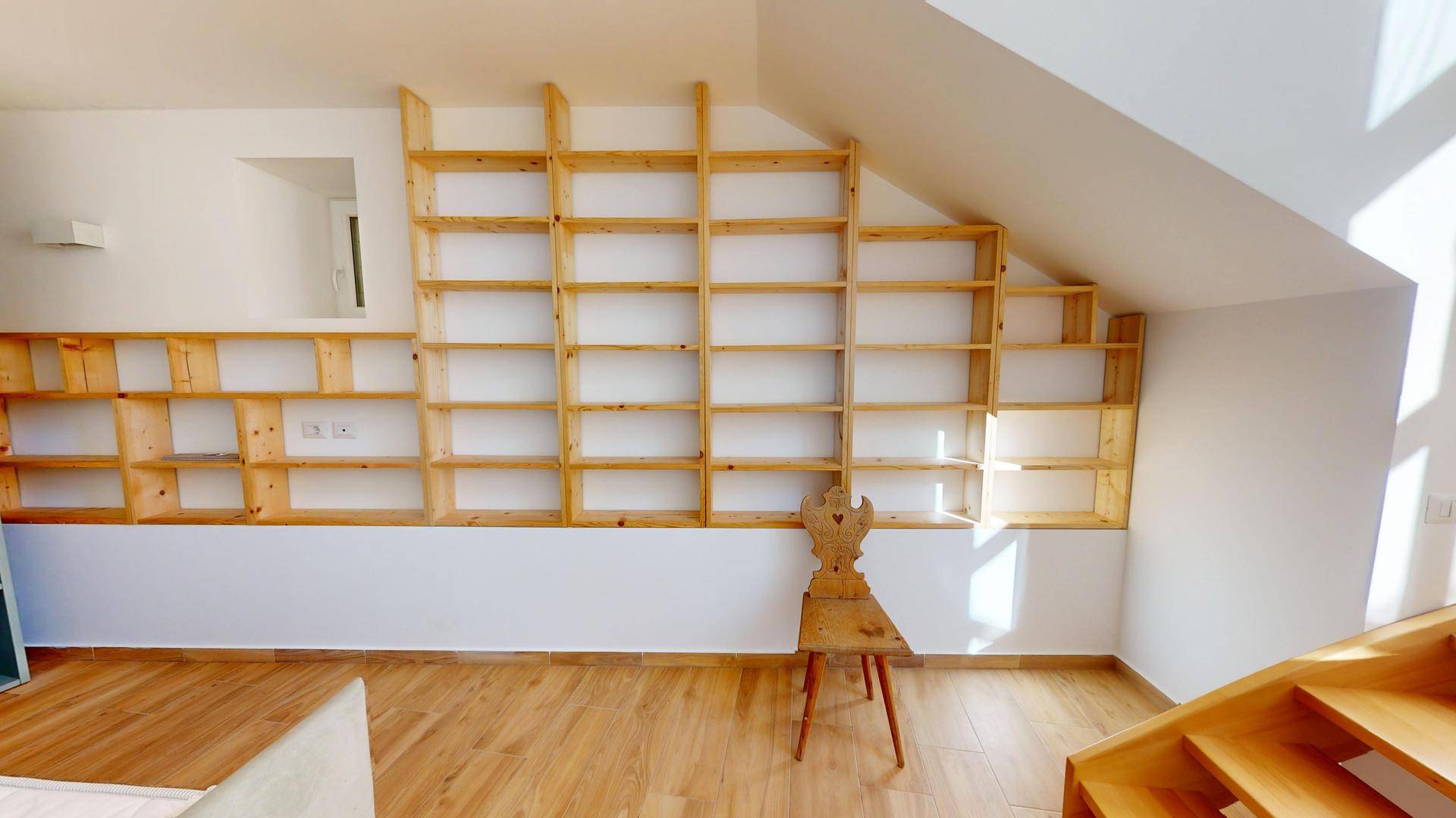 Maßgefertigtes Holzregalsystem, das sich der Dachschräge anpasst, mit einem traditionellen Holzstuhl.
