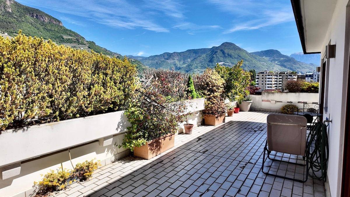 Geräumige Terrasse mit vielen Pflanzen und weitem Blick auf die Berge und die Stadt.
