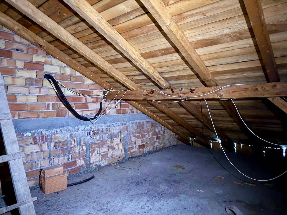 Dachbodenbereich mit freiliegenden Holzbalken und Ziegelwänden, bereit für Renovierung und Ausbau.