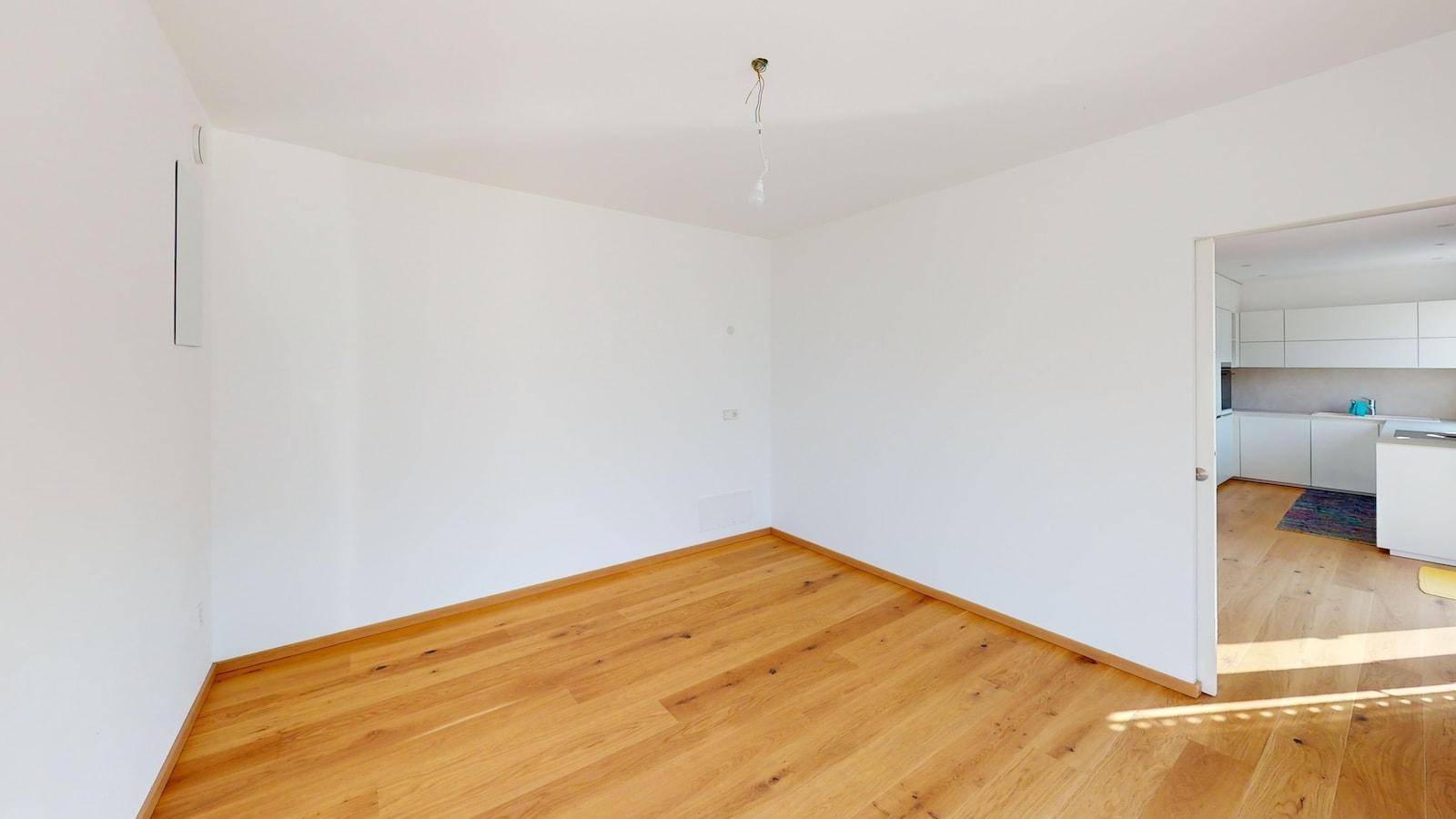 Heller, leerer Wohnbereich mit Holzboden und offenem Zugang zur Küche.
