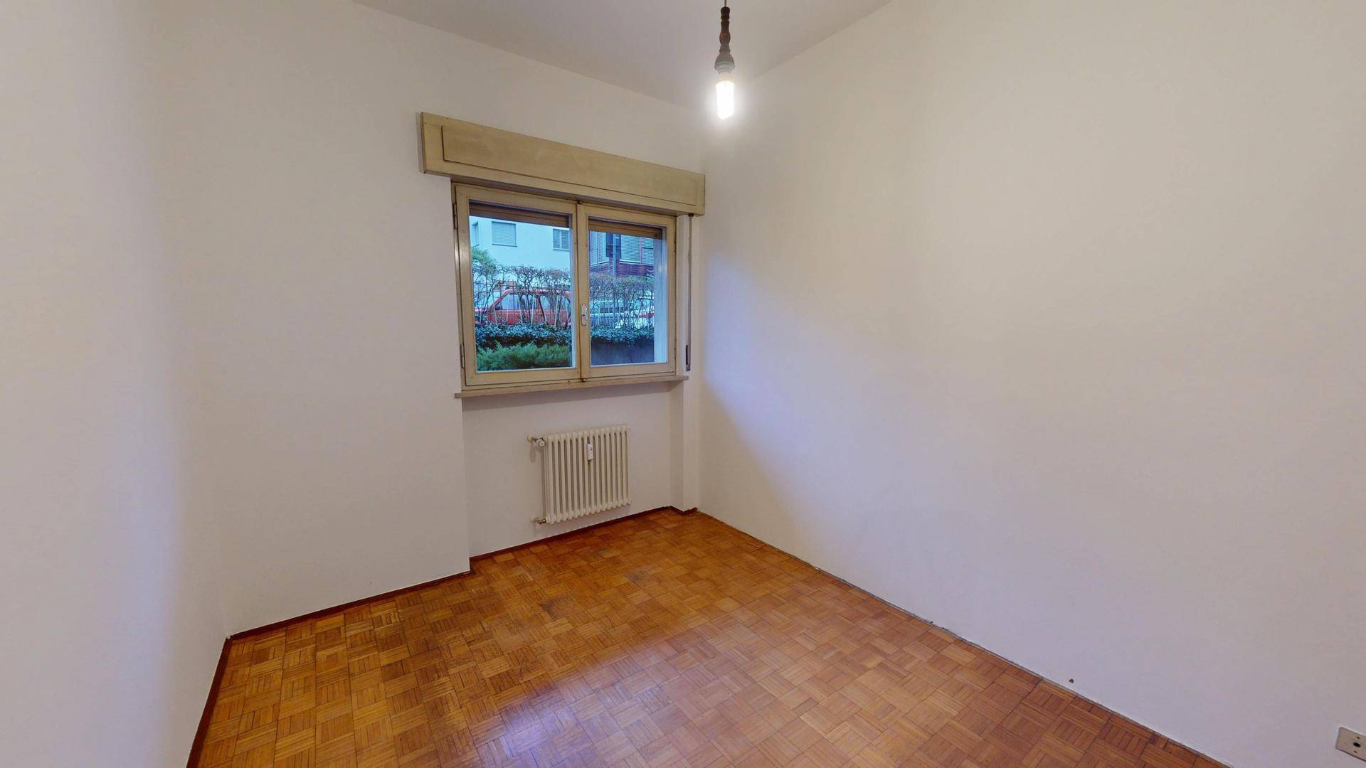 Ruhiges Zimmer mit Parkettboden und einem Fenster, das viel Tageslicht hereinlässt.