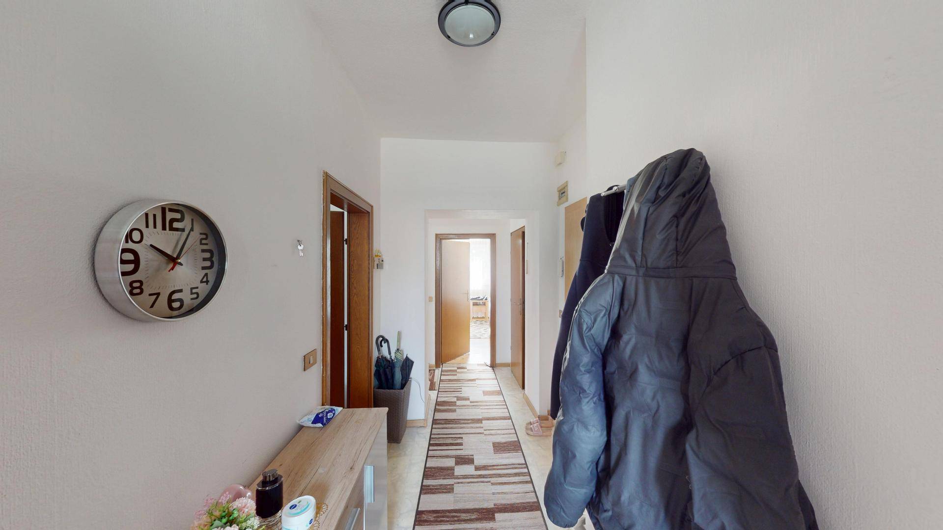 Langer Flur mit Garderobe, Fliesenboden und Türen zu verschiedenen Zimmern.