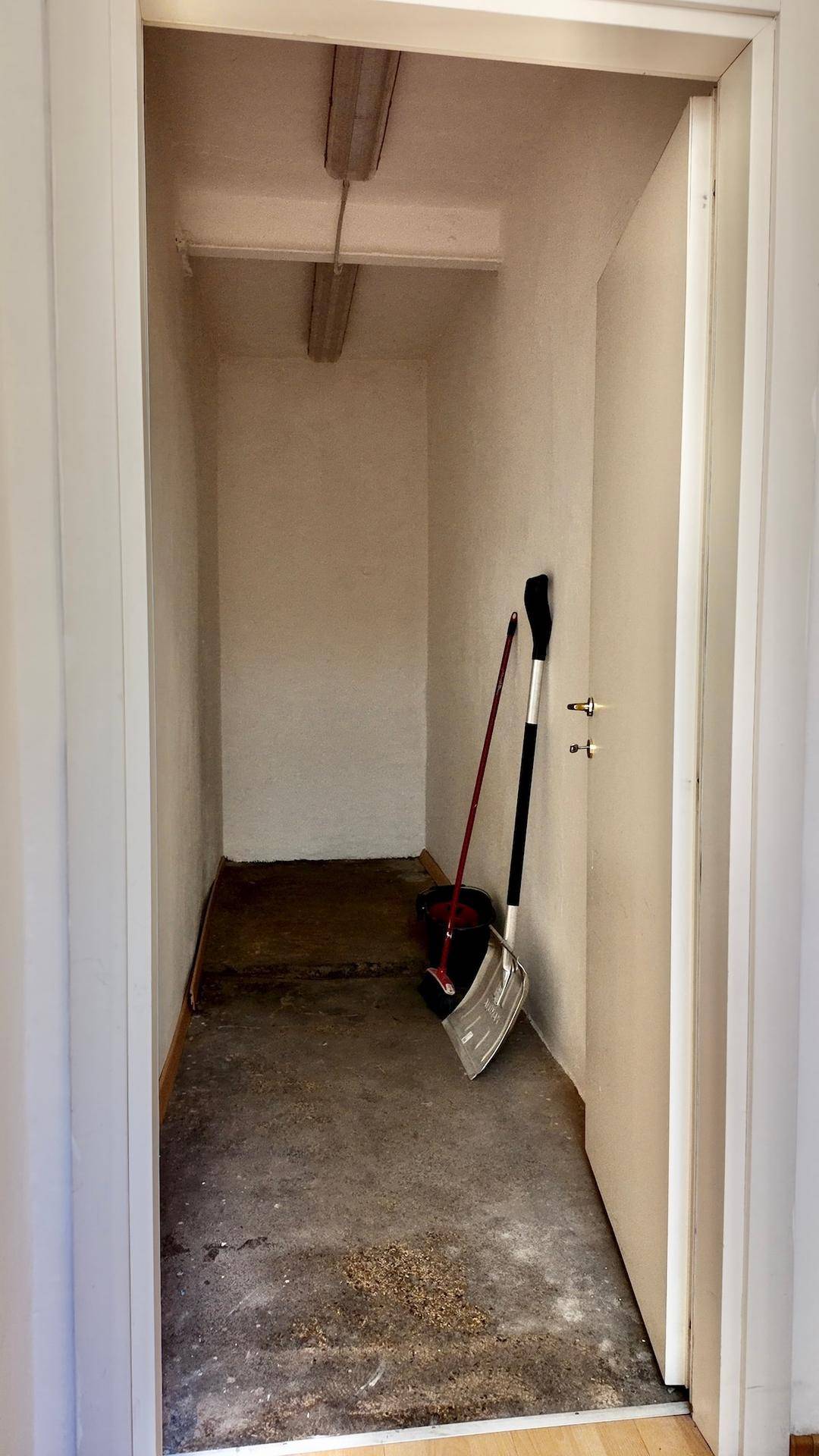 Kleiner Abstellraum mit Betonboden und Reinigungsgeräten, ideal für Lagerzwecke.