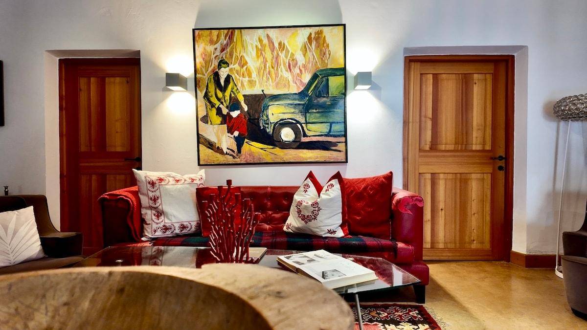 Gemütliches Wohnzimmer mit rotem Ledersofa, Couchtisch und farbenfrohem Kunstwerk über dem Sofa.
