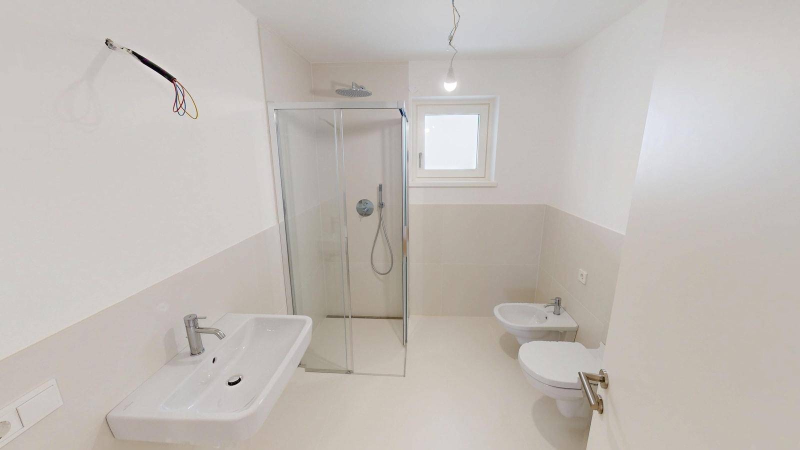 Modernes Badezimmer mit Dusche, Waschbecken, Bidet und WC, ausgestattet mit hellen Fliesen.