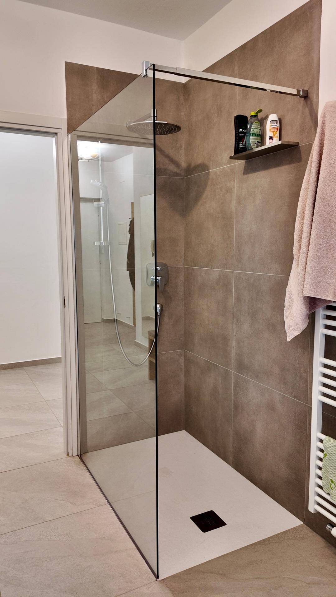 Geräumige begehbare Dusche mit Glasabtrennung, Regenduschkopf und modernen grauen Fliesen.