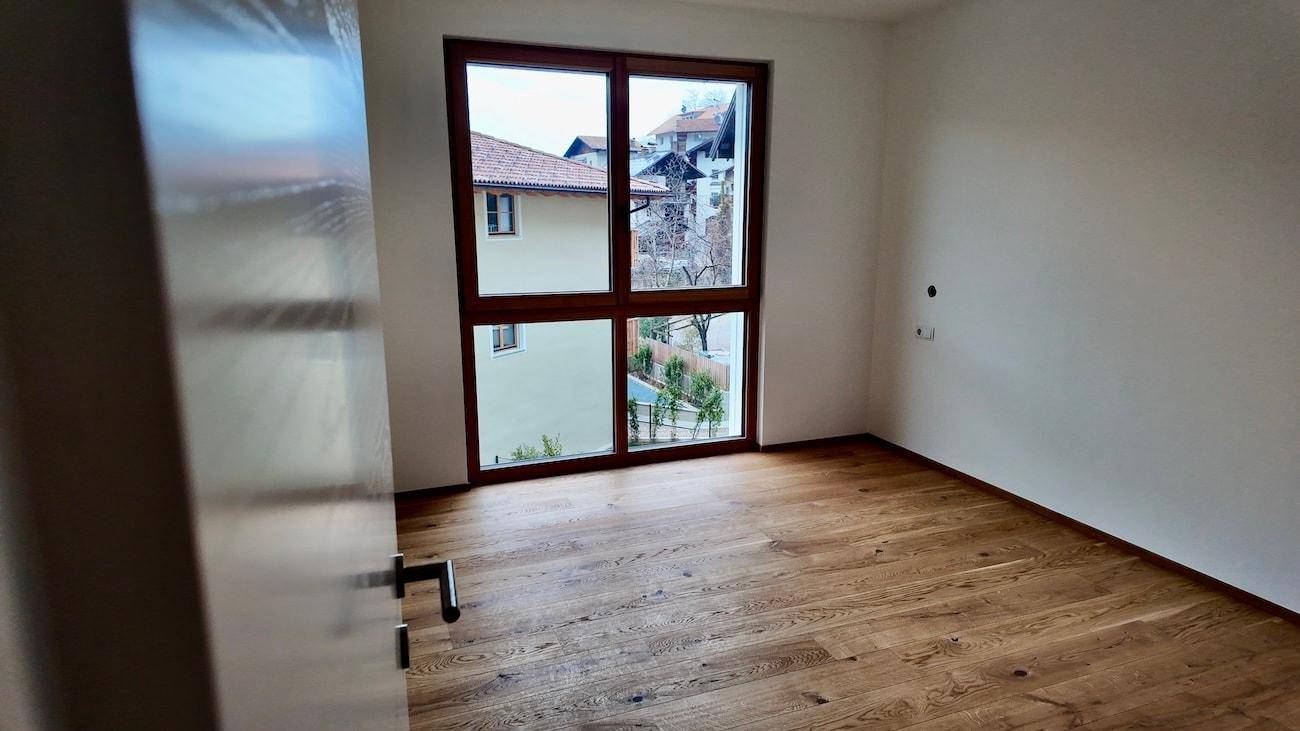 Helles, unmöbliertes Zimmer mit Holzboden und großem Fenster mit Blick auf die Umgebung.