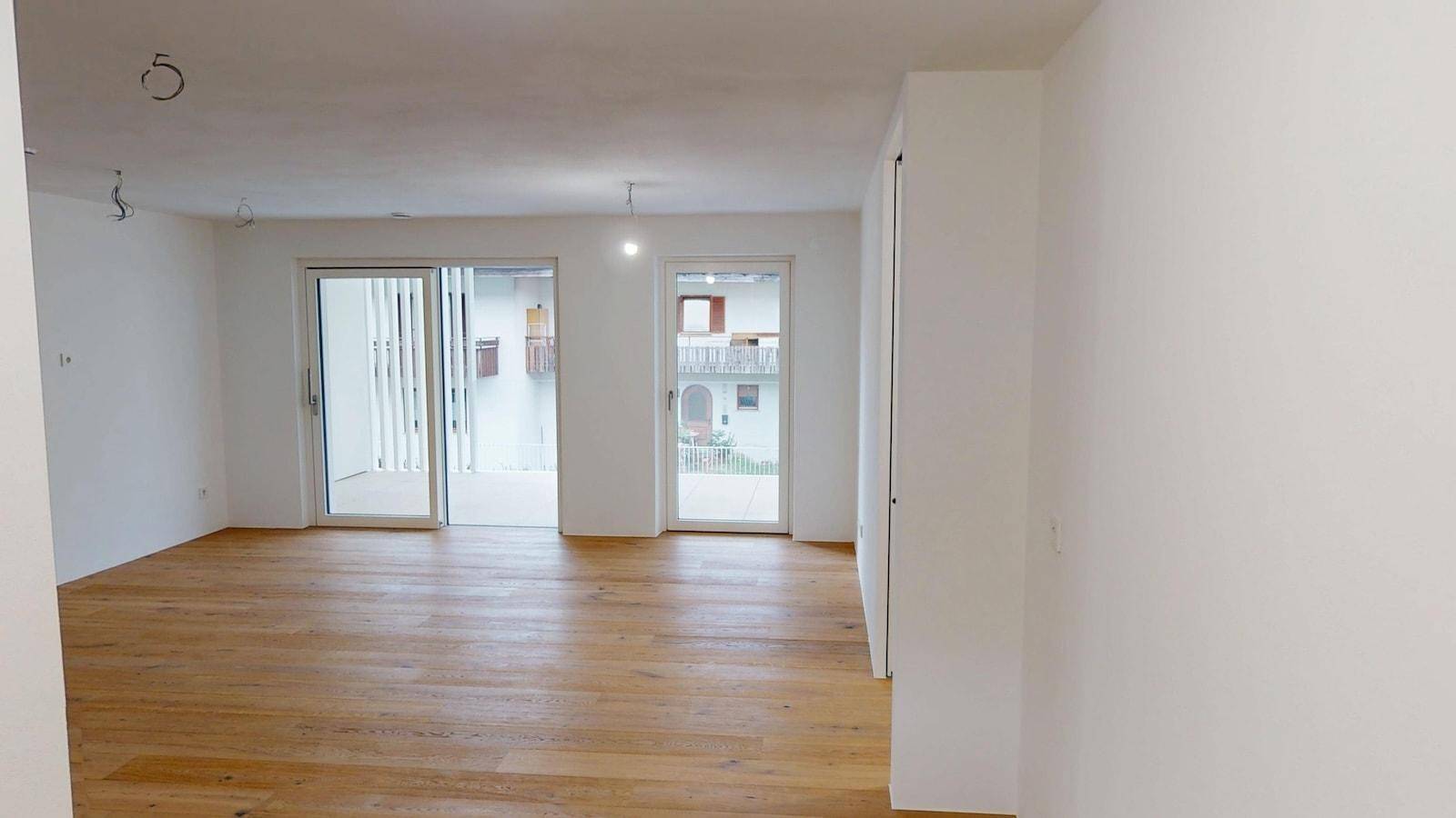 Geräumiger, heller Raum mit Holzboden und zwei Fenstertüren zu einem Außenbereich.
