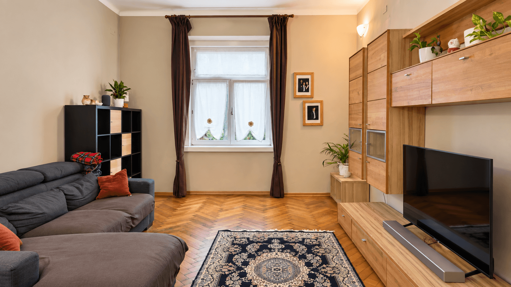 Helles Wohnzimmer mit beigen Wänden, Holzmöbeln und einem Teppich auf Parkettboden.