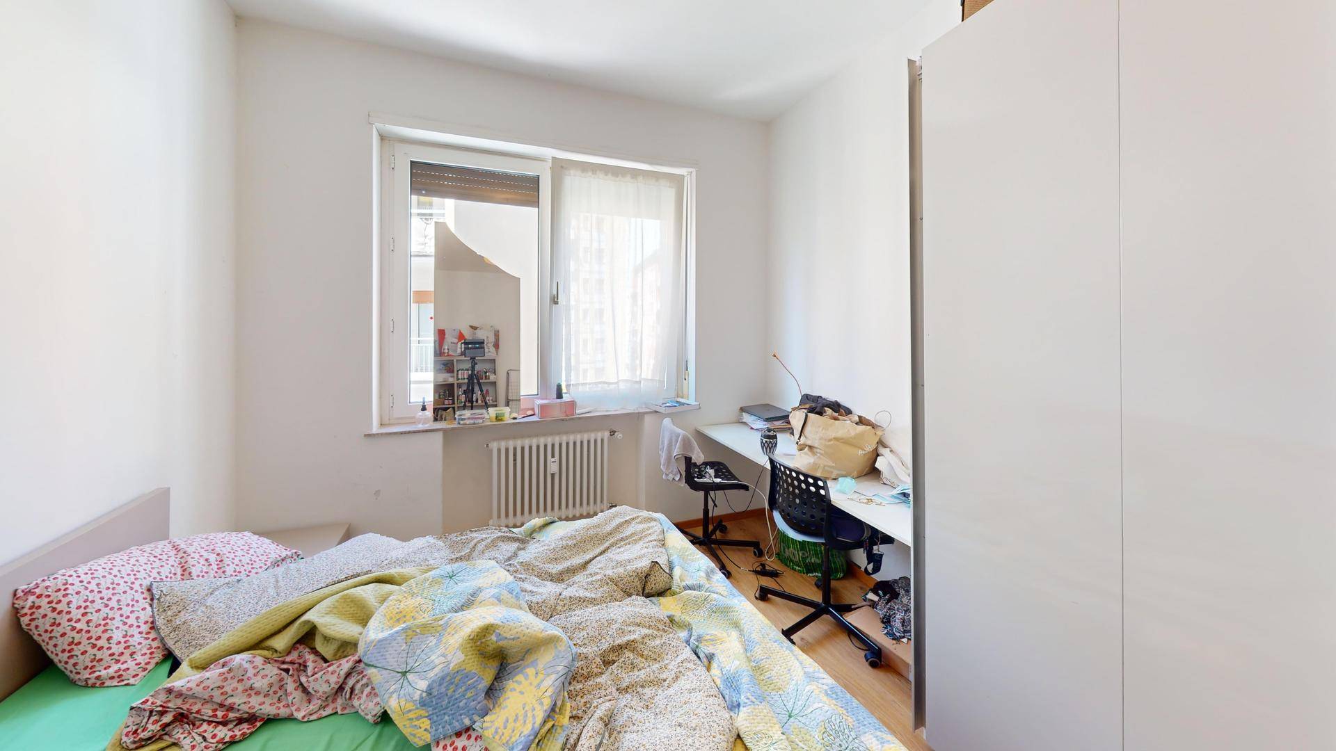 Schlafzimmer mit Holzboden, Bett und Schreibtisch am Fenster.