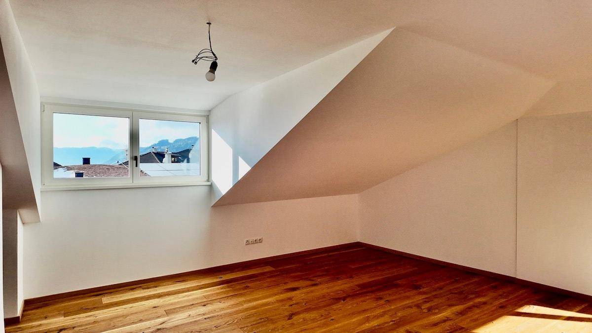 Helles Zimmer im Dachgeschoss mit Holzboden, schrägen Wänden und weitem Ausblick.
