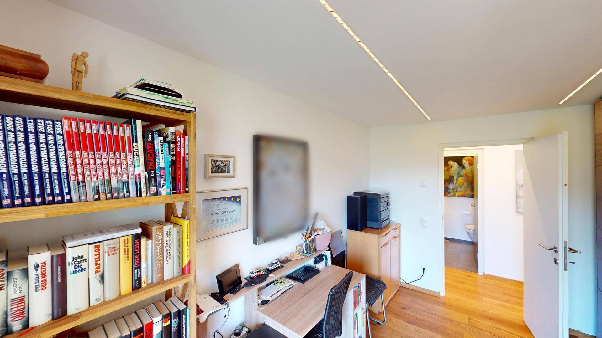 Arbeitszimmer mit Bücherregal, Schreibtisch und Zugang zu einem angrenzenden Badezimmer.