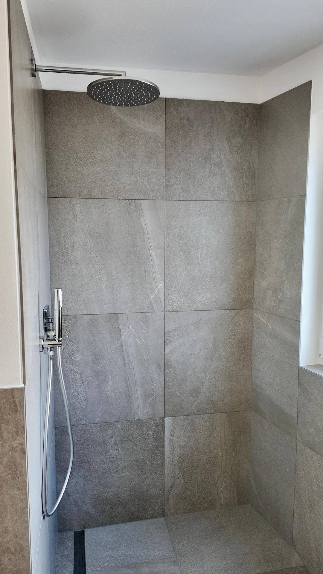Moderne Duschkabine mit großformatigen grauen Fliesen und Regenduschkopf.