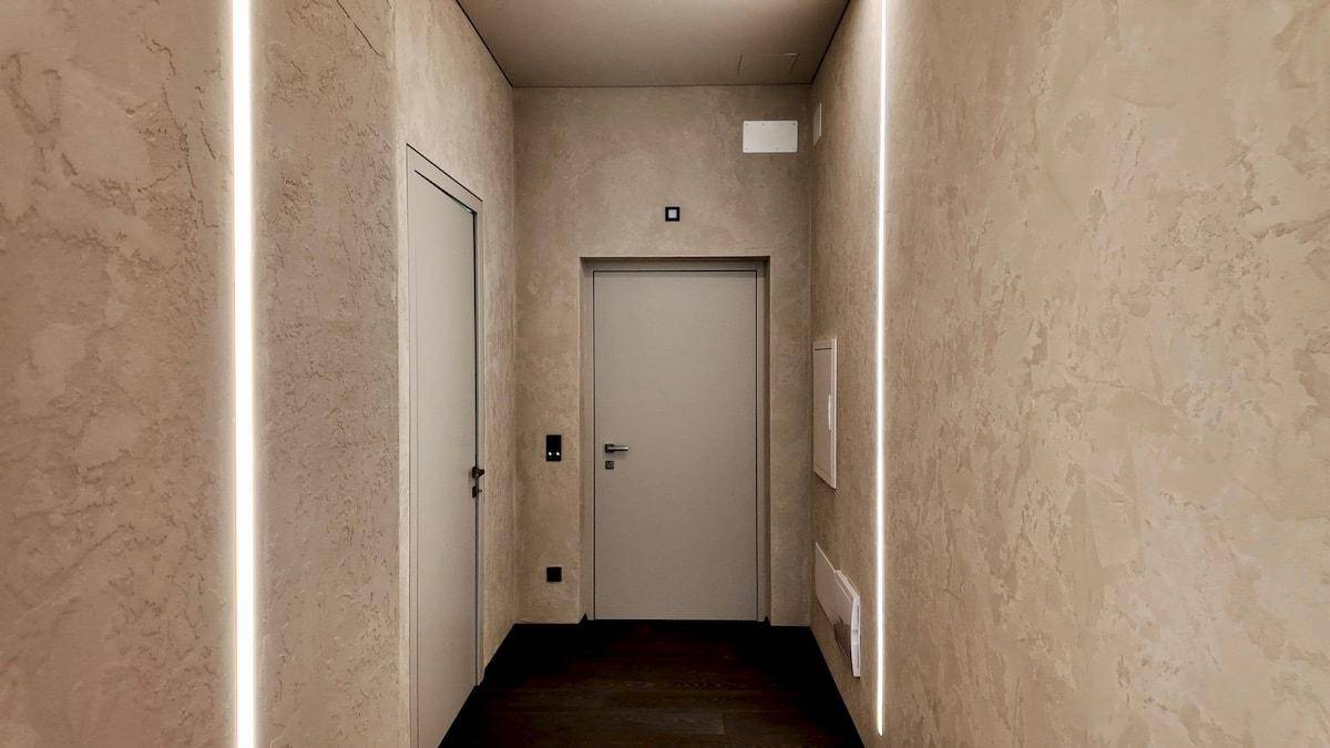 Moderner Flur mit hellen Wänden, dunklem Holzboden und stilvoller indirekter Beleuchtung.
