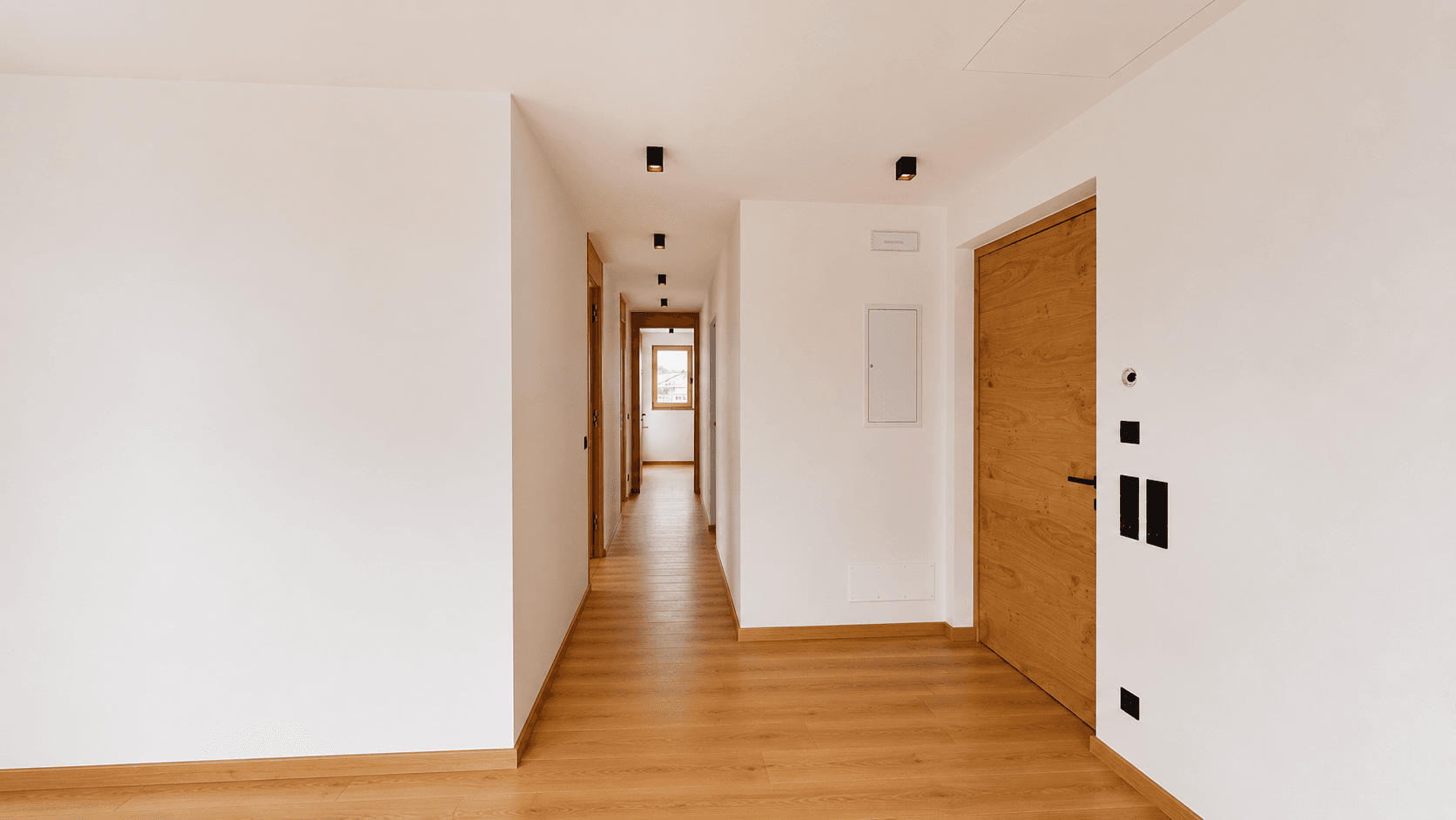 Langer, heller Flur mit Holztüren und durchgehendem Parkettboden.
