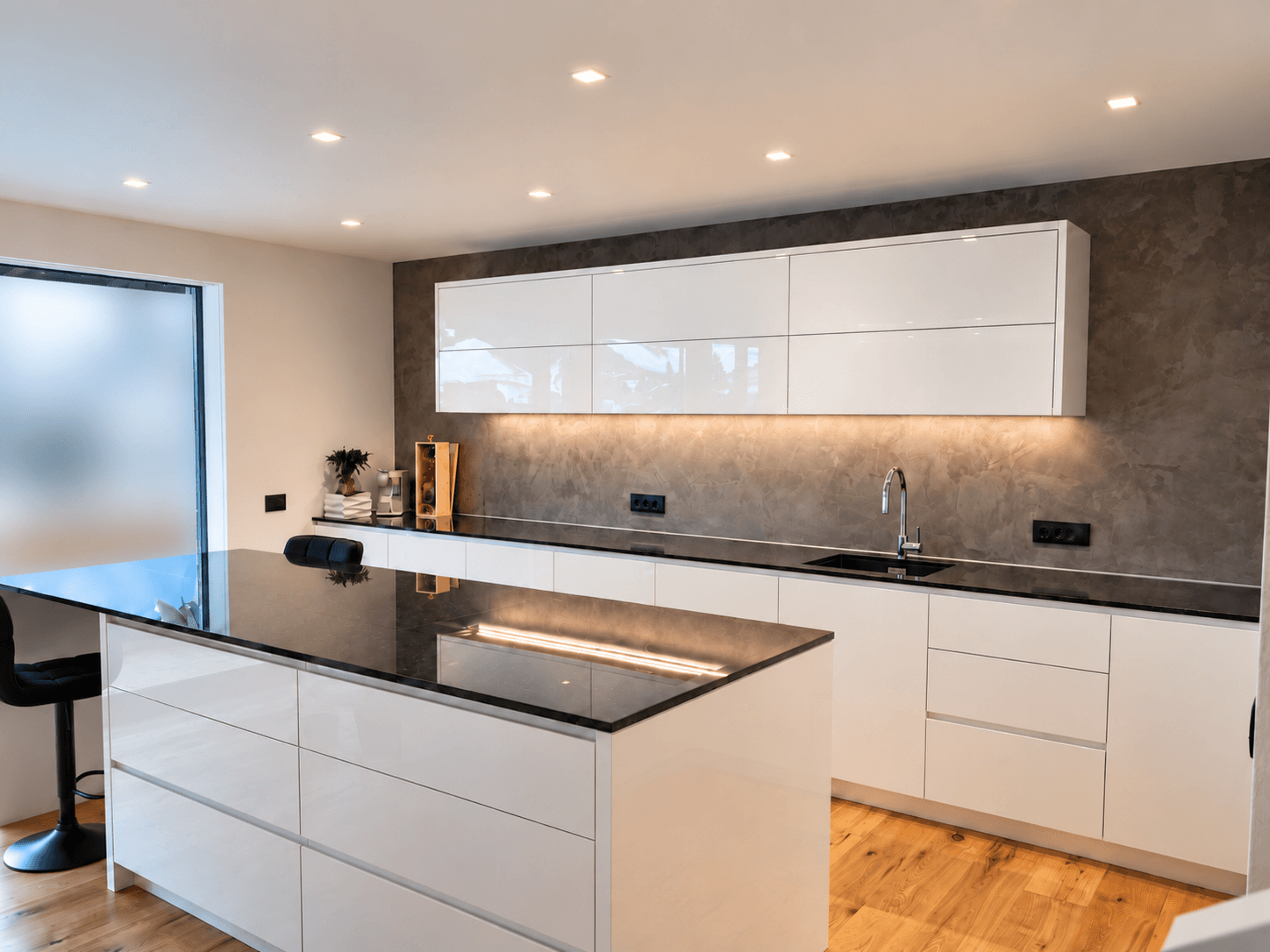 Elegante moderne Küche mit weißen Hochglanzfronten, schwarzen Arbeitsplatten und integrierter Beleuchtung.