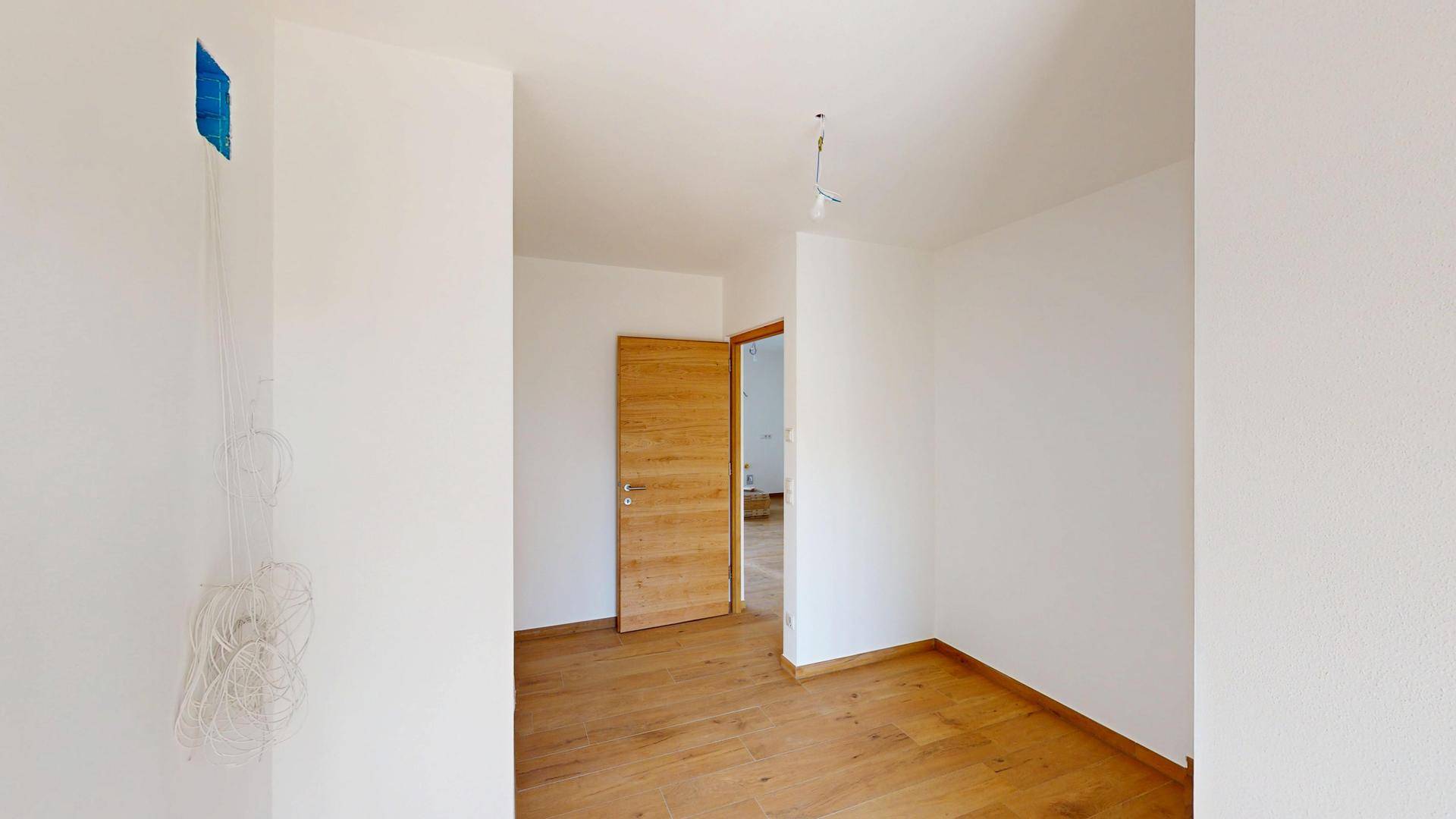 Unmöbliertes Zimmer mit hellem Holzboden und einer modernen Holztür.