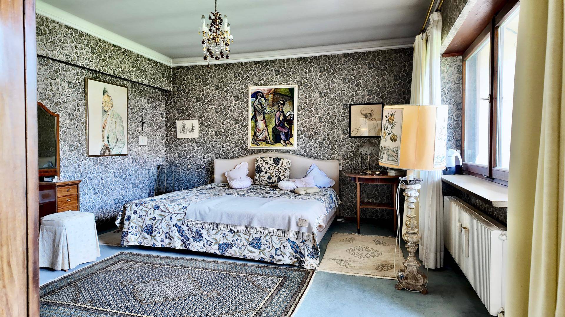 Geräumiges Schlafzimmer mit gemusterten Tapeten, Teppichboden und traditionellen Möbeln.