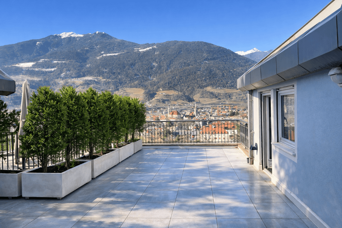 Große, leere Dachterrasse mit Fliesenboden und weitem Blick auf die Stadt und Berge.