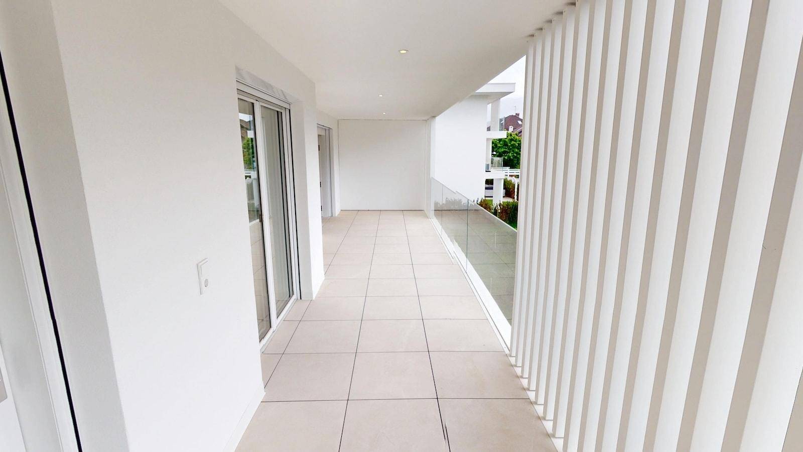 Langer, moderner Balkon mit Fliesenboden und Glasgeländer, ideal für Entspannung im Freien.