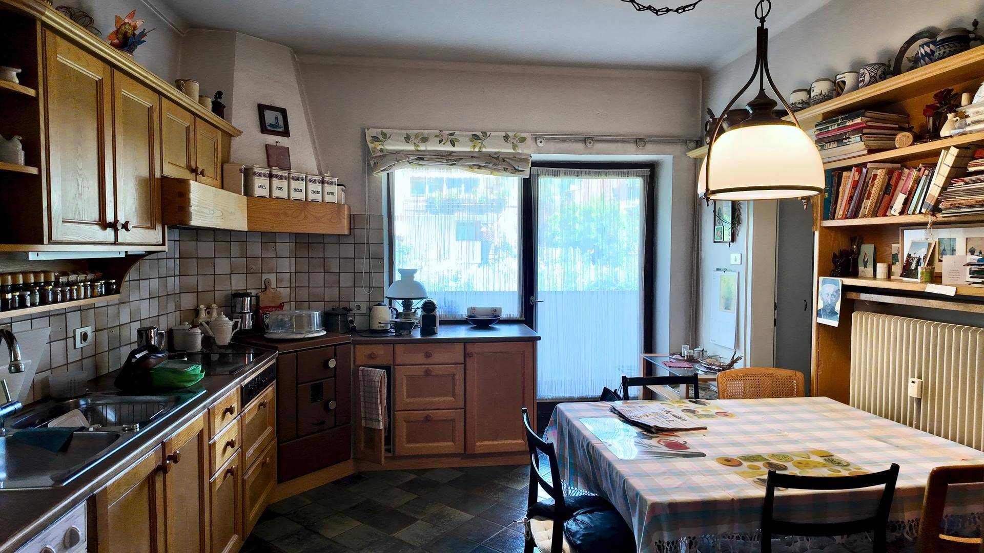 Gemütliche Küche mit Holzeinbauten, Esstisch und Fenster mit Blick nach draußen.