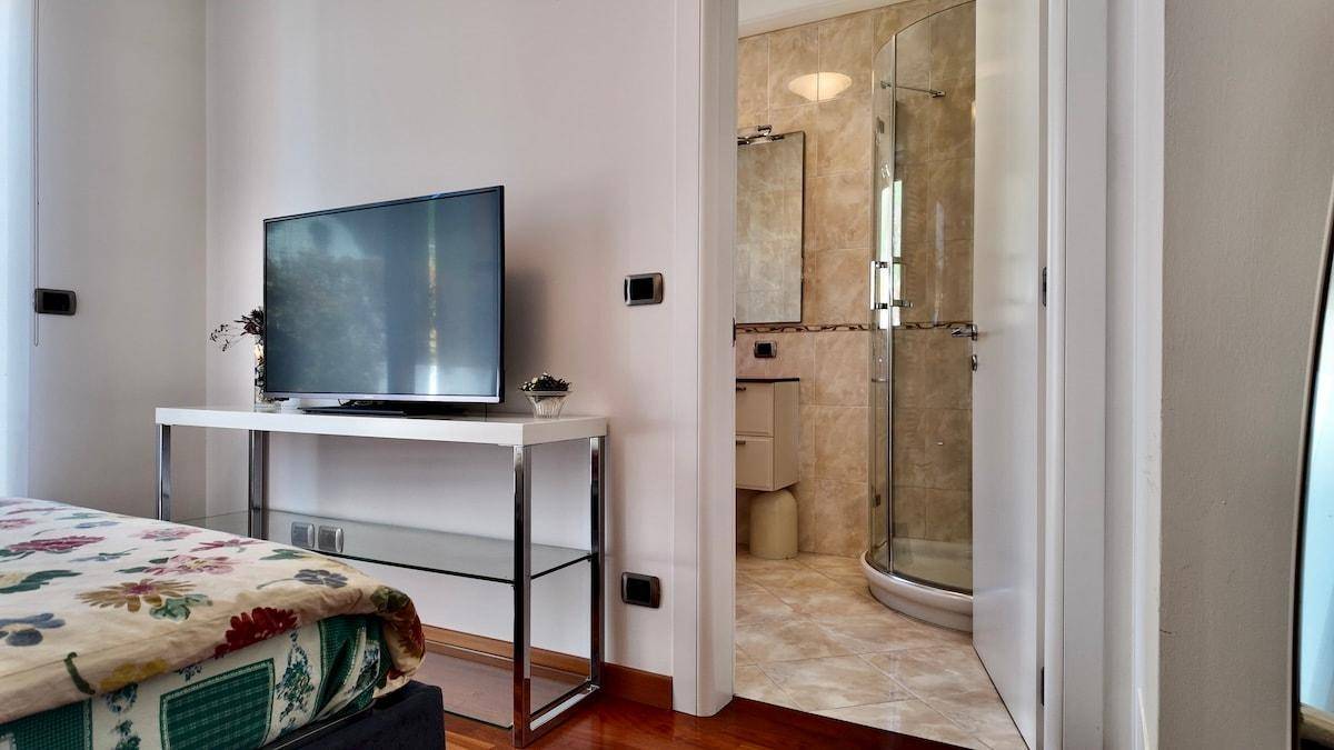 Schlafzimmer mit Holzboden und Zugang zu einem modernen Badezimmer mit Dusche.