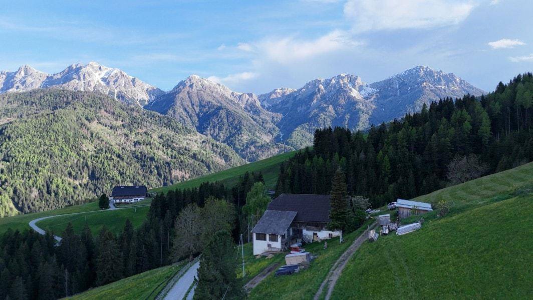 Ländliches Anwesen mit traditionellen Gebäuden in einer grünen Hügellandschaft mit majestätischen Bergen.