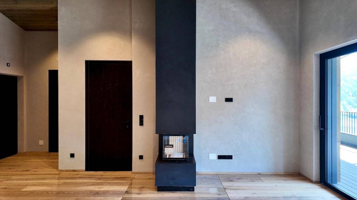 Moderner Kamin als Blickfang in einem hellen Raum mit Holzboden und dunkler Tür.