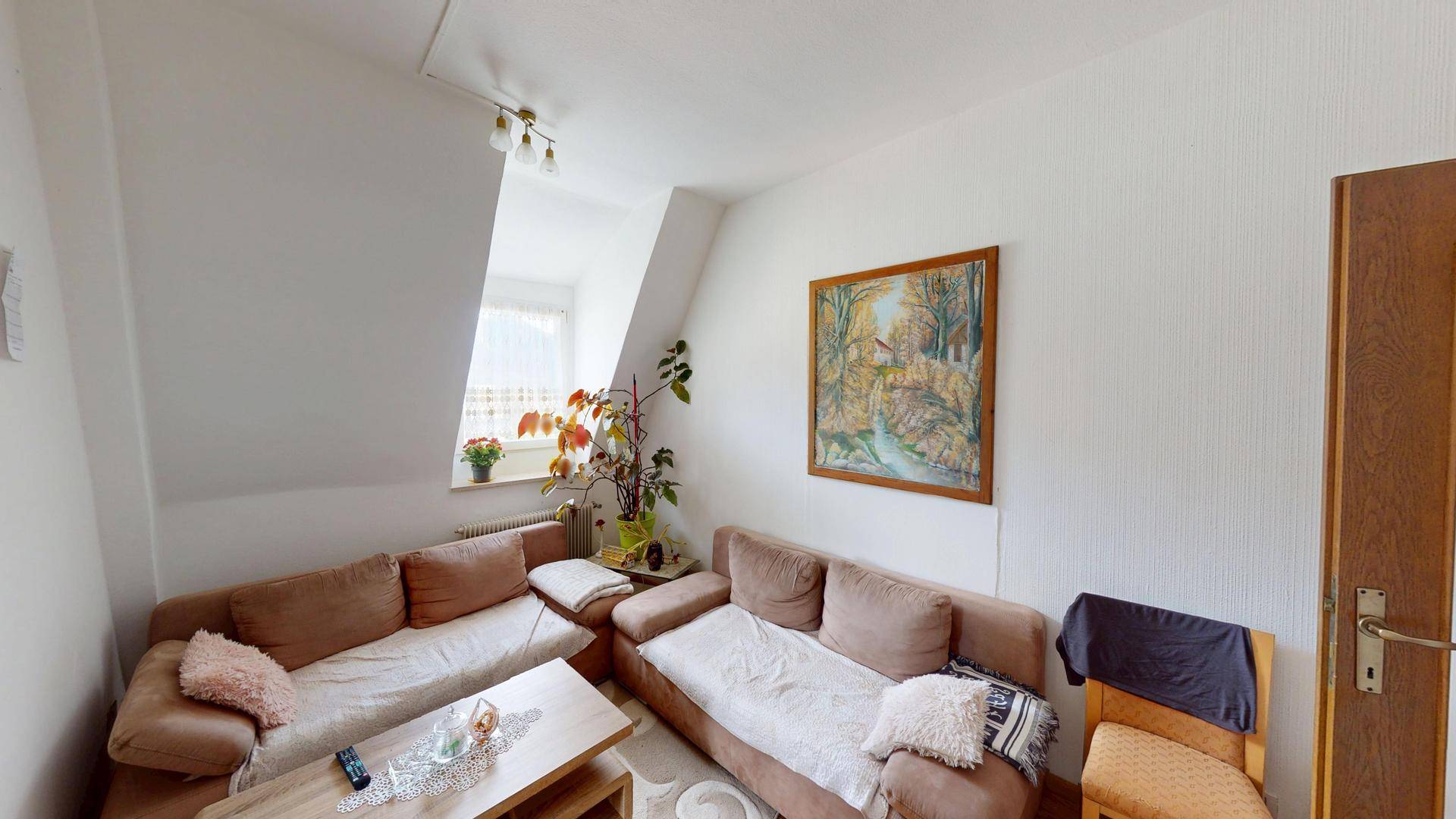 Helles Wohnzimmer mit Dachschrägen, einem großen Sofa und einem Fenster für natürliches Licht.