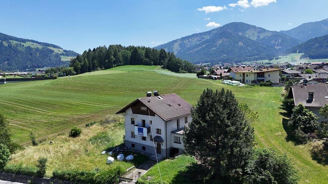 Haus in idyllischer Lage umgeben von grünen Hügeln und einer malerischen Bergkulisse.