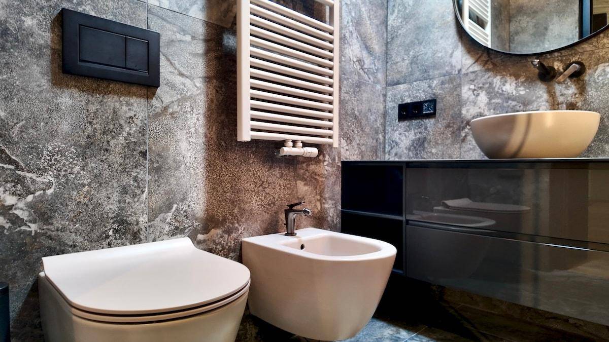 Elegantes Badezimmer mit Wand-WC, Bidet, Handtuchheizkörper und großformatigen grauen Fliesen.